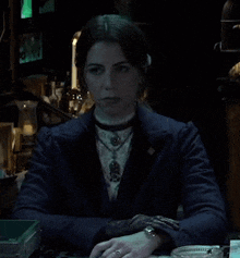 a woman in a blue jacket is sitting at a table in a dark room