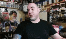 a bald man with a tattoo on his arm is sitting in front of a shelf full of toys .