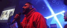 a man in a red hoodie is singing into a microphone in a dark room .