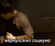 a man in a brown shirt is dancing in a dark room with a caption in russian .