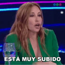 a woman in a green jacket is holding a glass of water and saying esta muy subido