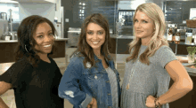 three women standing next to each other in a kitchen smiling