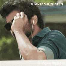 a man wearing sunglasses and ear buds is talking on a cell phone with the website starttamilchat.in visible