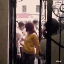 a woman in a yellow sweater is standing in a doorway in front of a group of people