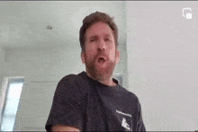 a man with a beard is wearing a black t-shirt and making a face .