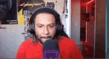 a man wearing headphones and a red shirt is talking into a microphone in a room .