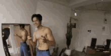 a man without a shirt is standing in front of a mirror in a living room .