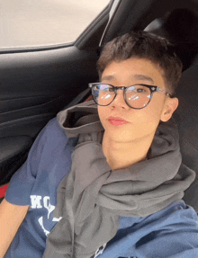 a young man wearing glasses and a blue shirt that says kc