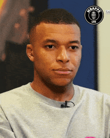 a man is wearing a gray shirt with a microphone and a logo that says mbappe live on it