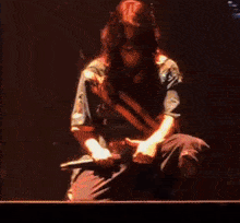 a man with long hair is kneeling on a stage holding a microphone .