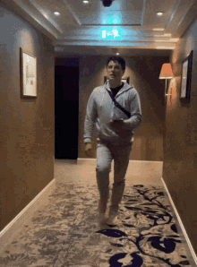 a man is walking down a hallway with a blue exit sign above him