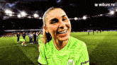 a woman in a green shirt with the letter w on it is smiling on a soccer field