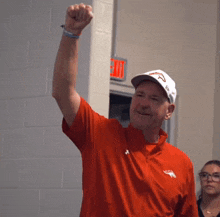 a man wearing a red shirt and a white hat has his fist up in the air