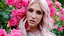 a woman with pink hair and gloves is surrounded by pink roses in a garden .
