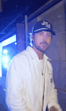 a man with a beard wearing a white jacket and a blue hat that says i 'm not out .