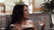 a woman sitting on a couch holding a glass of wine and says good luck