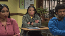 a woman sits at a desk with her arms crossed while a man sits in a blue sweatshirt