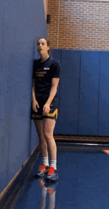 a woman is leaning against a wall in a gym while wearing shorts .