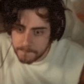 a man with a beard wearing headphones and a white shirt is looking at the camera .