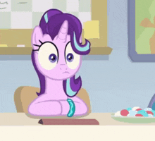 a cartoon pony is sitting at a table with a plate of candy in front of her .