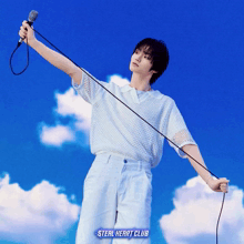 a man is holding a microphone in front of a blue sky with the words steal heart club on the bottom