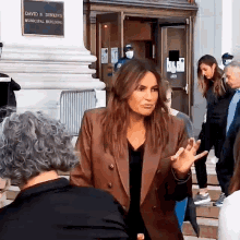 a woman in a brown jacket is standing in front of a david n. dinkins municipal building