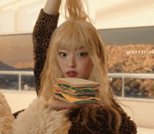 a woman in a leopard print top holds a sandwich in front of a hollywood sign