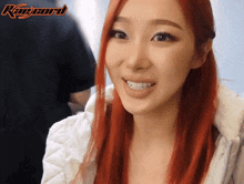 a woman with red hair is smiling in front of a sign that says kae card