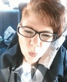 a woman wearing glasses and a black jacket is sitting in a car seat