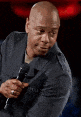 a bald man in a suit is holding a microphone and wearing a ring on his finger