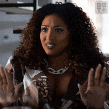 a woman with curly hair is wearing a leopard print shirt and a necklace that says be it