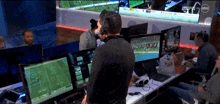 a man wearing a headset stands in front of a computer monitor with a football game on it