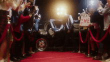 a man is getting out of a car on a red carpet with a sign that says " kat me "
