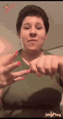 a woman in a green tank top with pink nails is making a gesture with her hands ..