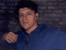 a man in a blue hoodie is standing in front of a brick wall