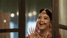 a close up of a woman in a wedding dress laughing while looking out of a window .