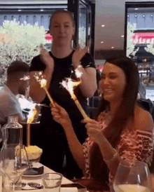two women are holding sparklers in their hands while sitting at a table .