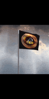 a black flag with a gold emblem on it is waving in the wind against a cloudy sky