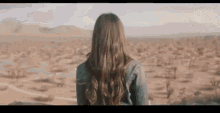 a woman is standing in the middle of a desert looking at the landscape .