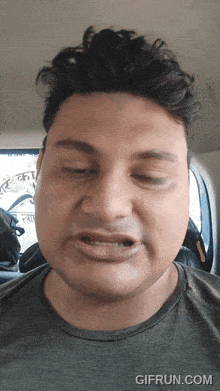 a man is making a funny face in a car with gifrun.com written on the bottom