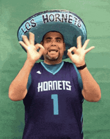 a man wearing a sombrero and a hornets jersey giving an ok sign