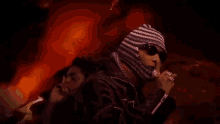 a man wearing a beanie and sunglasses is singing into a microphone .