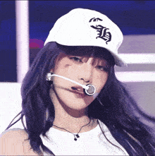 a woman with purple hair wears a white hat with the letter h on the front