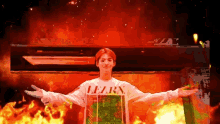 a man wearing a shirt that says lelry is standing in front of a fire