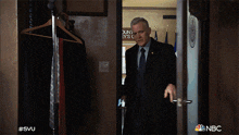 a man in a suit and tie is standing in a doorway with the nbc logo on the bottom right
