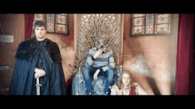 a man in a cape is standing next to a man sitting on a throne with a sword