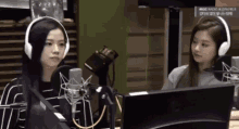 two women wearing headphones are sitting in front of a computer monitor
