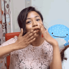 a woman covering her mouth with her hands while sitting in front of a stuffed animal