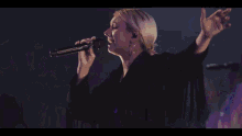a woman sings into a microphone in front of a crowd of people