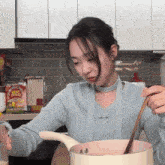 a woman in a blue sweater stirs a pot with a wooden spoon in front of a box of lucky charms cereal